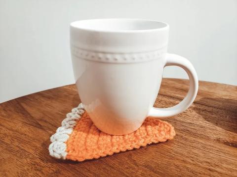 A cup sitting on a crochet pumpkin pie coaster